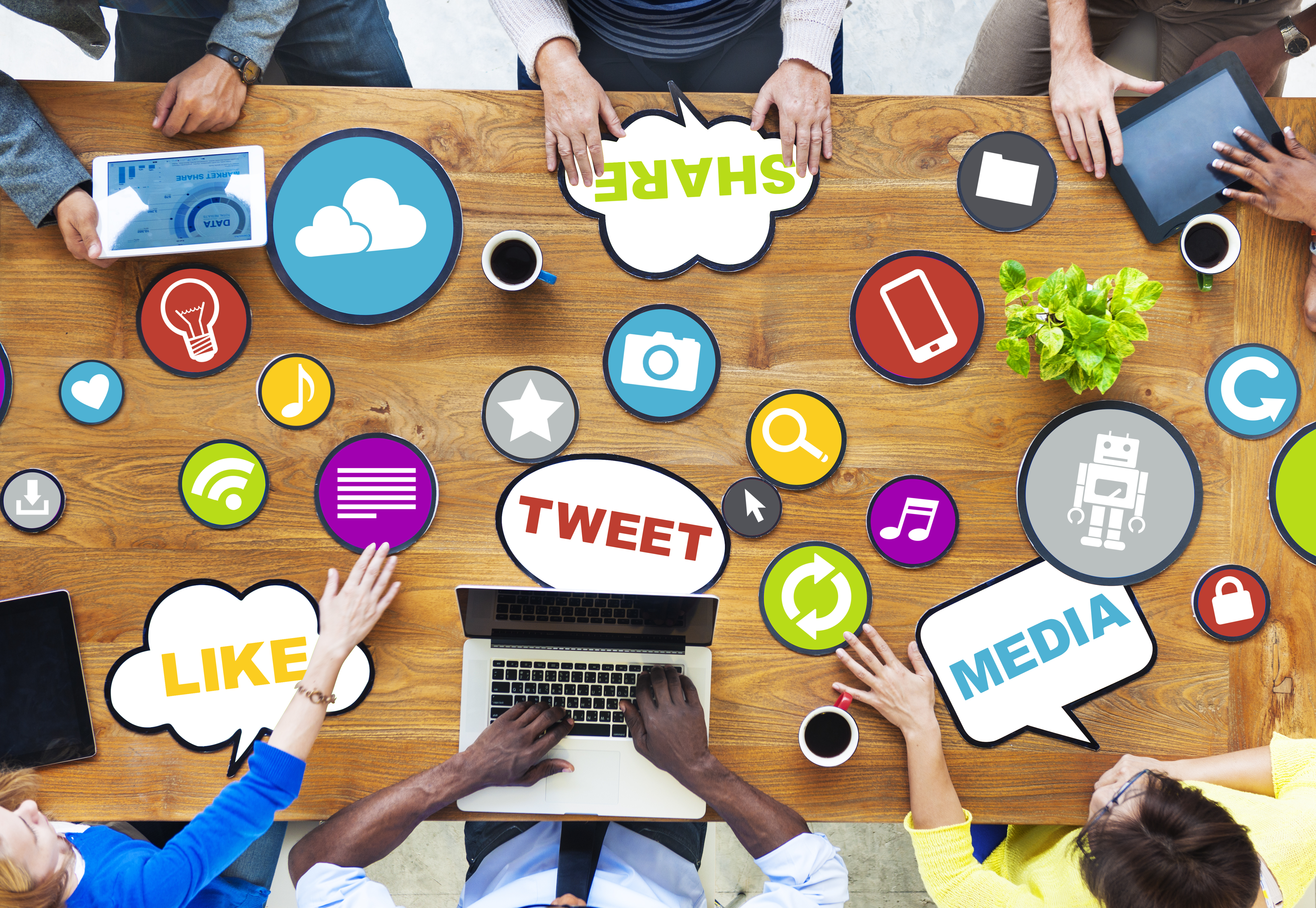 people working on various devices at a table with various social media icons and phrases